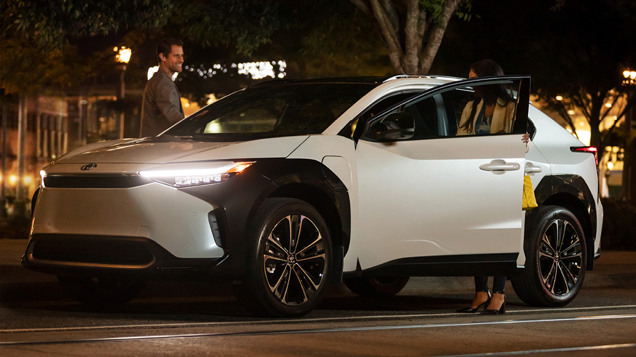 Vue latérale du Toyota BZ4x stationné en soirée avec un couple entrant dans la voiture