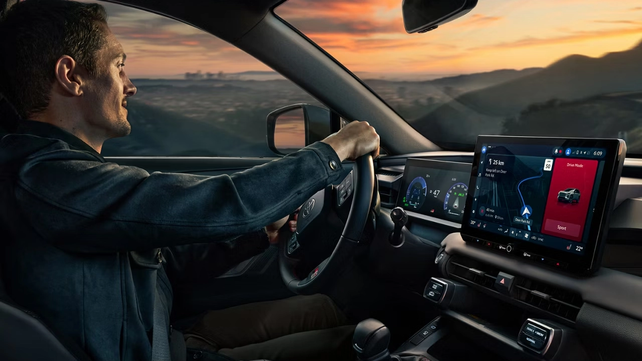 Interior of the Toyota RAV4, featuring a large touchscreen display showing navigation, set against a backdrop of a sunset landscape
