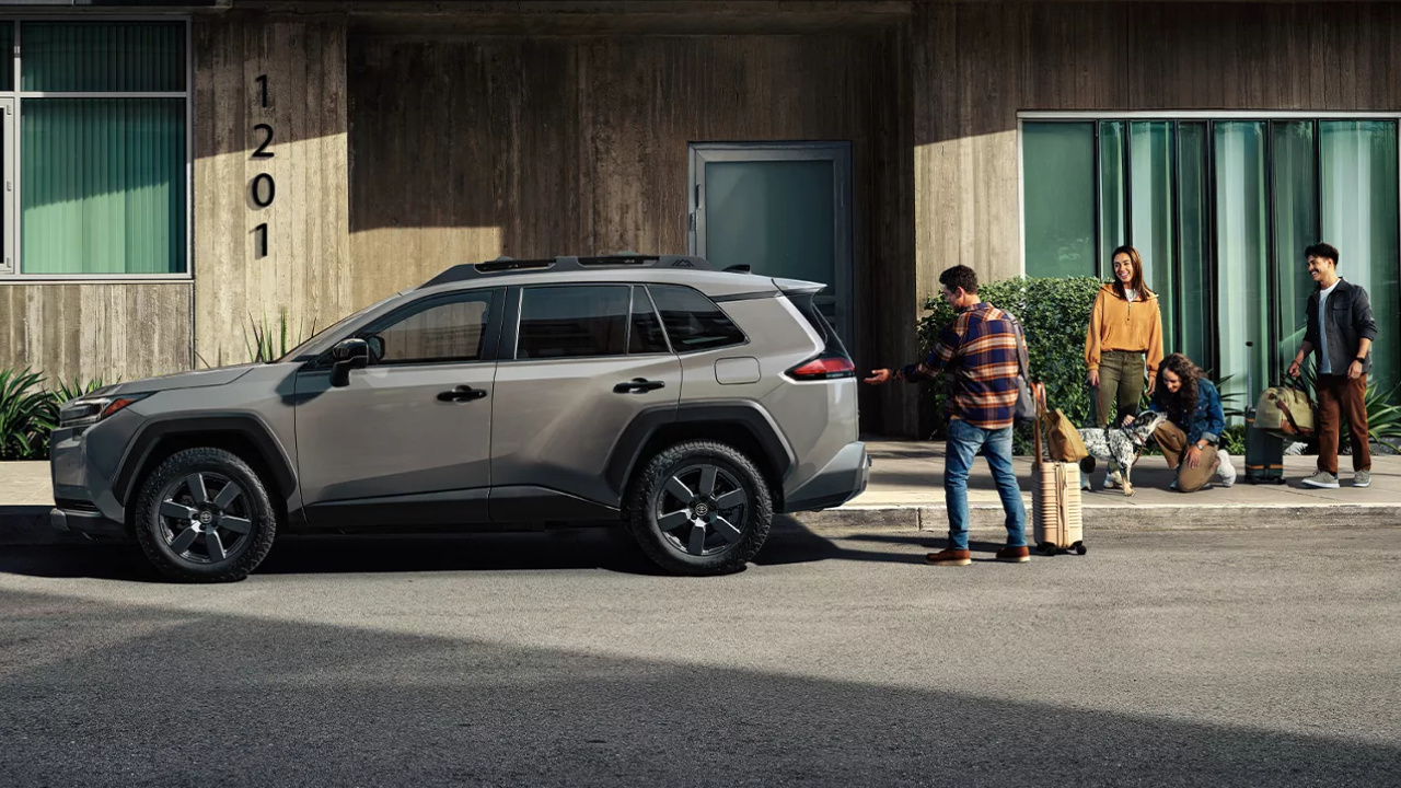 Toyota RAV4 2026 gris stationné devant un bâtiment, avec deux personnes à proximité.