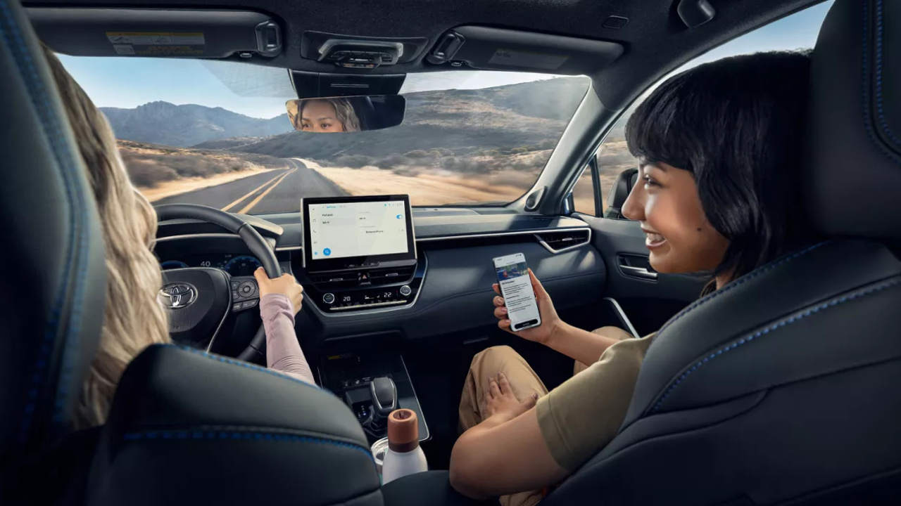 Conductrice et passagère à bord du Toyota Corolla Cross hybride 2026, avec écran central et téléphone.
