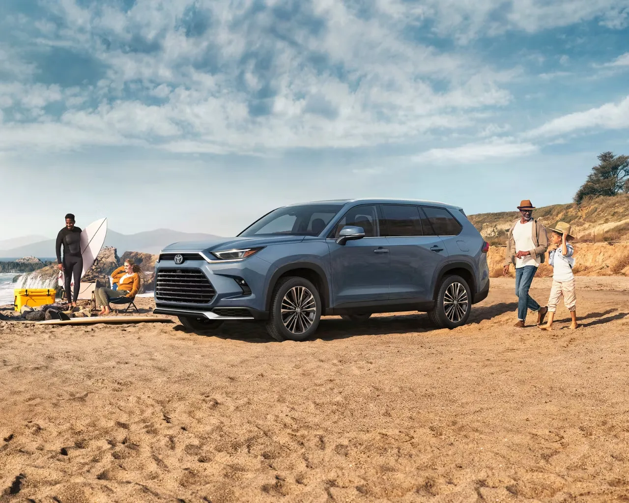 2026 Toyota Grand Highlander Hybrid parked at the beach with a family, illustrating the choice of a 7-seat SUV.