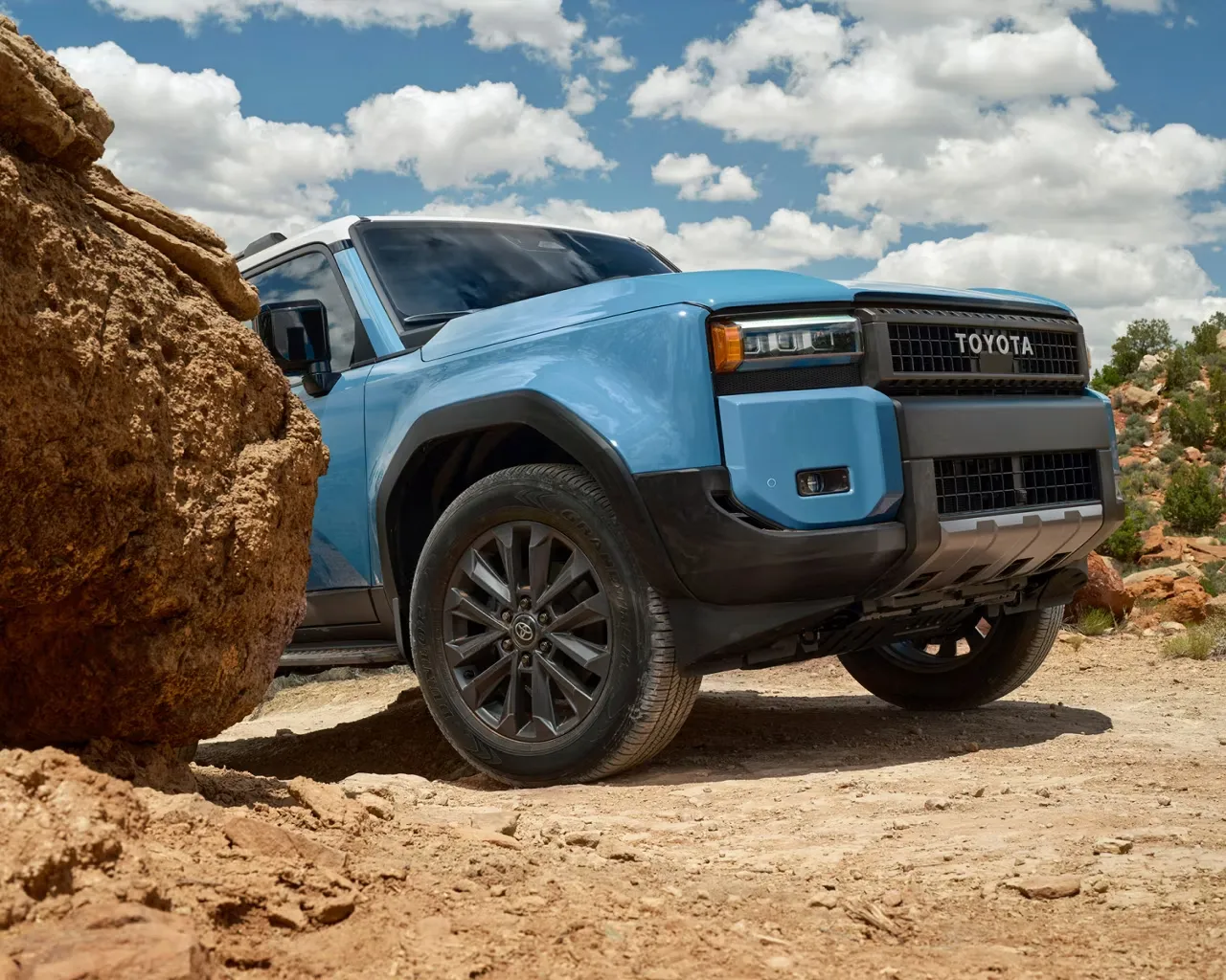 Blue 2027 Toyota Land Cruiser viewed from the front three-quarter angle on rocky terrain.